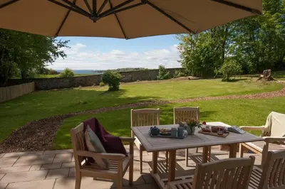a wooden table with chairs and an umbrella on a patio at Beltie Lodge in Borgue