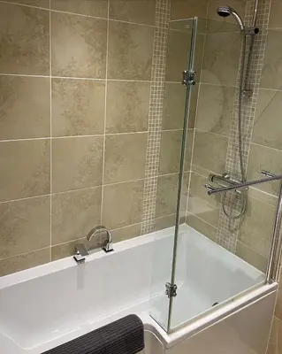 a shower with a glass door next to a bath tub at Flosh Cottage Lake District in Cleator