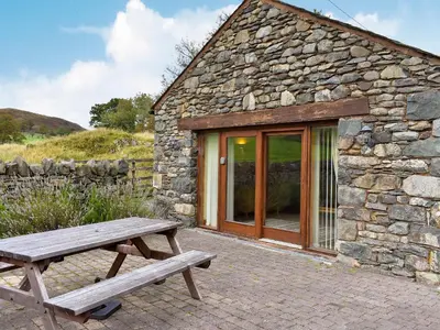 a wooden picnic table next to a stone building at Hilltoft Barn in Dockray