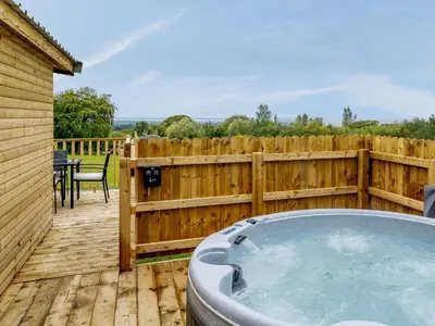 a hot tub on a wooden deck with a fence at Starling Lodge - Uk31071 in Westward