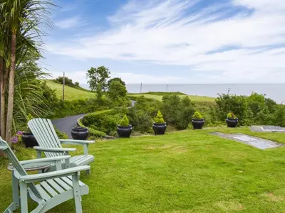 two white chairs sitting on a lawn with a road at Seacliffe in Kildonan