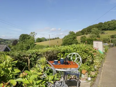 a table and chair in a garden with bushes and trees at Fellside Cottage in Cockermouth