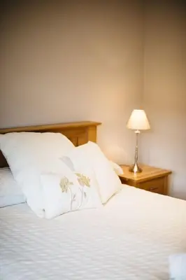 a bed with white pillows and a table with a lamp at Waterfront Apartments in Douglas