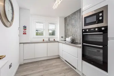 a kitchen with white cabinets and a clock on the wall at 9A Millbrae - Donnini Apartments in Ayr
