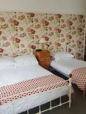two beds in a bedroom with floral wallpaper at Dorchester House in Keswick