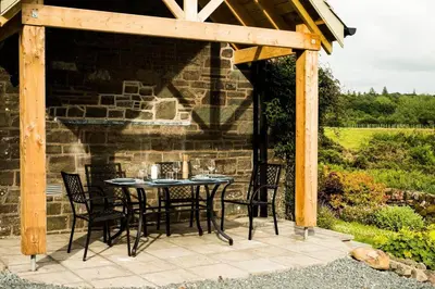 a patio with a table and chairs under a wooden pergola at Culdoach in Castle Douglas