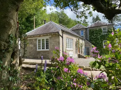 a stone house with flowers in front of it at Stables Cottage in Langholm