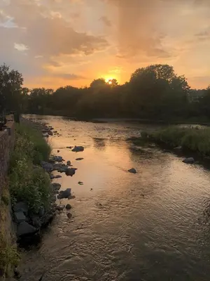 a river with rocks and the sunset in the background at Daffodil House in Cockermouth