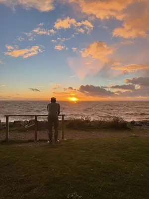 a man standing next to a fence watching the sunset at Immaculate 2-Bed Lodge in Monreith in Newton Stewart