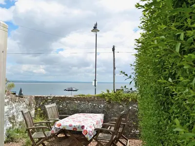 a table and chairs with an umbrella and the ocean at Coastguard's Cottage in Carsethorn