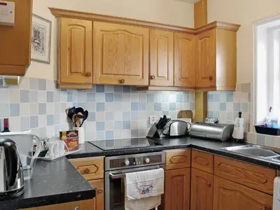 a kitchen with wooden cabinets and a stove top oven at Coastguard's Cottage in Carsethorn
