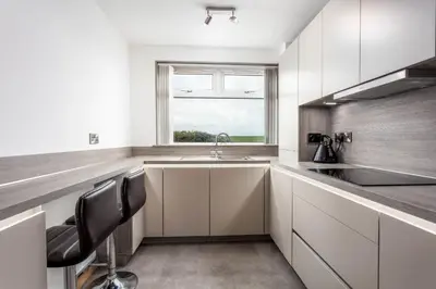 a kitchen with white cabinets and a sink and a window at West Sands - Donnini Apartments in Ayr