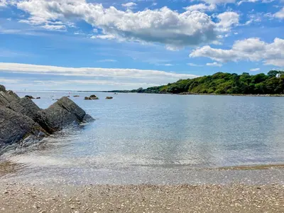 a beach with rocks in the water and trees at Kerrim Cottage in Ringford
