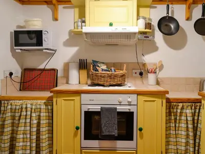 a kitchen with yellow cabinets and a stove top oven at Church Cottage in Rigg