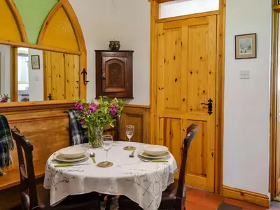 a dining room with a table with a vase of flowers at Church Cottage in Rigg