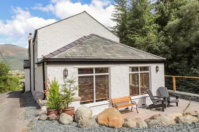 a small white house with a bench and some rocks at Ladstock Cottage in Keswick