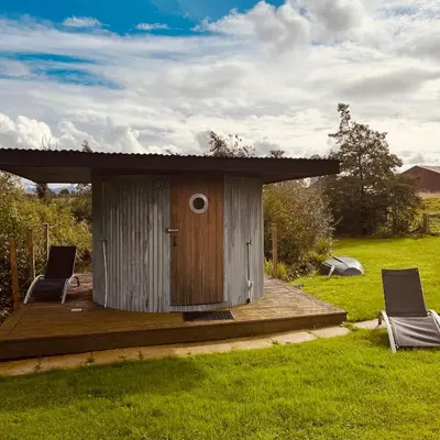 a wooden out house with two chairs in a field at The Dairy in Castle Douglas