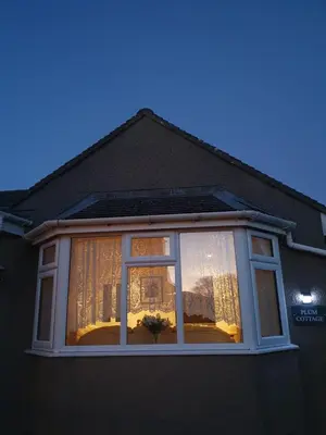 a window on the side of a house with curtains at Plum Cottage in Keswick