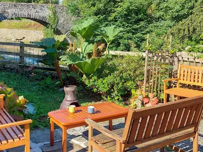 a patio with a table and a bench and a vase at Riverside Cottage in Keswick