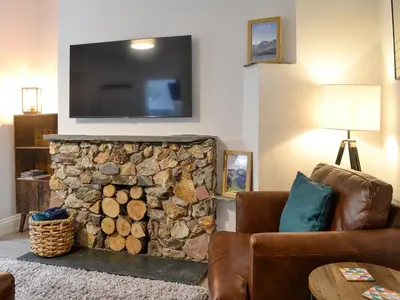 a living room with a stone fireplace with a flat screen tv at Howbeck Cottage in Hesket Newmarket