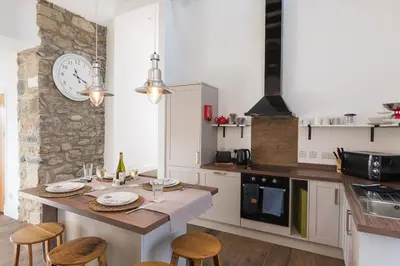 a kitchen with a table with chairs and a clock on the wall at Grobdale Byre in Gatehouse of Fleet