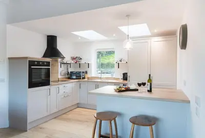 a kitchen with white cabinets and a blue island with stools at Croft Cottage in Gatehouse of Fleet