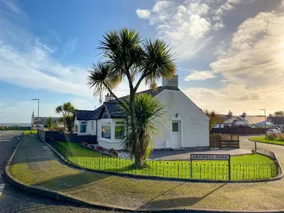 a house with a palm tree next to a fence at Ardwell Park in Ardwell