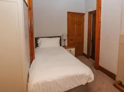 a bedroom with a white bed with a wooden headboard at Old School Muncaster House in Ravenglass
