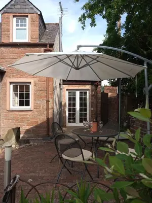 a table and chairs under an umbrella on a patio at Laurieknowe Coach House in Dumfries