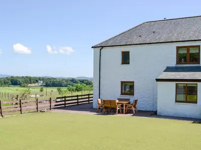 a white house with a table and chairs in front of it at The Byre - Camp Douglas - Cottage in Crossmichael