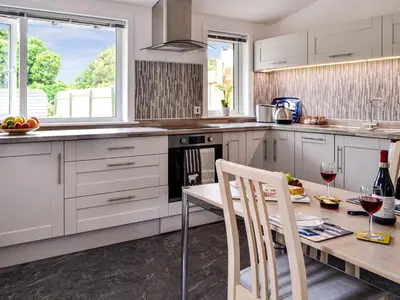 a kitchen with white cabinets and a wooden table with chairs at Park Crescent - Cottage in Creetown