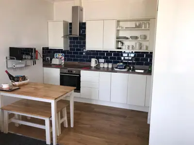 a kitchen with white cabinets and a wooden table at Curlew Cottage and Sunset View in Port Logan
