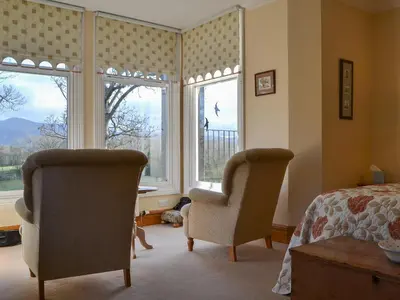 a bedroom with two chairs and a bed and windows at Middle Howe in Portinscale