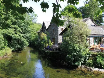 a building next to a river with people sitting on a bridge at Fir Tree Cottage in Ambleside