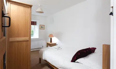 a bedroom with a white bed with a red pillow on it at Pollys Cottage in Elterwater