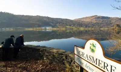 two people sitting on a stone wall near a lake at Thimble Hall in Grasmere