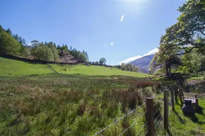 a fence and a bench in a field with a mountain at Robins Nest in Coniston
