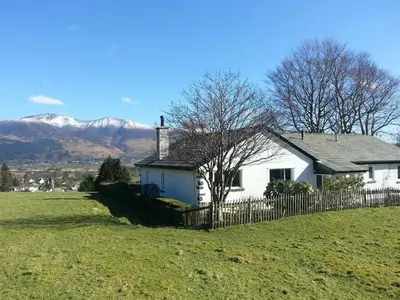 a white house in a field with mountains in the background at Bandol in Braithwaite