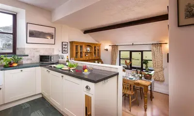 a kitchen with white cabinets and a dining room with a table at Thirlmere Cottage in Keswick