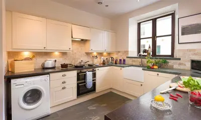 a kitchen with white cabinets and a washer and sink at Thirlmere Cottage in Keswick
