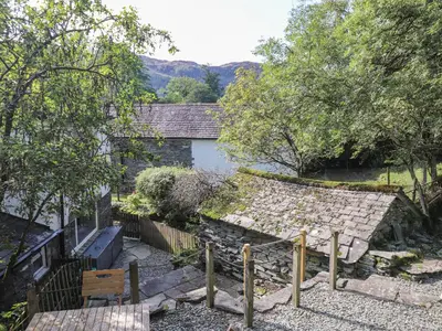 an external view of a cottage with a stone wall and trees at Weir Cottage in Ambleside