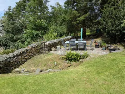 a table and chairs in a garden with a stone wall at Wythebank in Ambleside