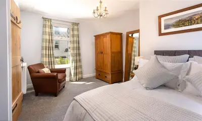 a bedroom with a bed and a chair and a window at Little Leveret Cottage in Keswick