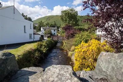 a small stream in front of a white building and a house at Gable End in Keswick