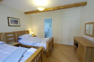 a bedroom with two beds and a desk and a room with two tables at Pen Cottage in Keswick