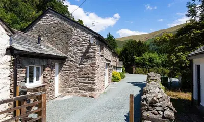 an old stone building with a stone wall next to a road at Underhowe in Grasmere