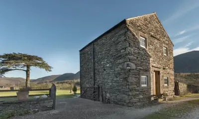 an old stone building with a tree and mountains in the background at Cedar Nook in Loweswater