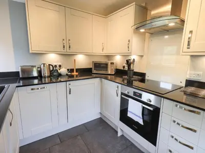 a kitchen with white cabinets and black counter tops at The Smithy in Borrowdale Valley