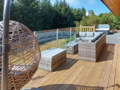 a deck with a couch and chairs on it at Treetops Luxury Log Cabin - Hot tub, BBQ & Sauna in Kippford