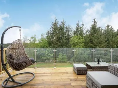 a basket swing on a patio with a fence at Treetops Luxury Log Cabin - Hot tub, BBQ & Sauna in Kippford